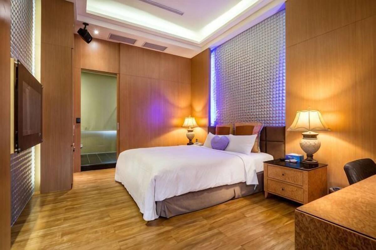 A hotel room with a bed, bedside lamps, a nightstand, a wooden floor, and a wall with a textured pattern.