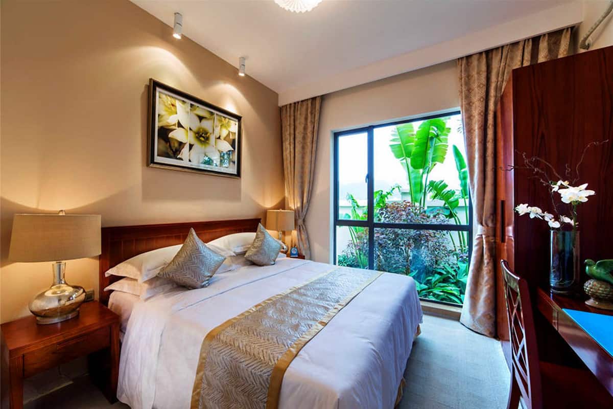 Habitación de hotel con una cama grande, dos mesitas de noche, un ventanal con vistas a zonas verdes y un cuadro en la pared.