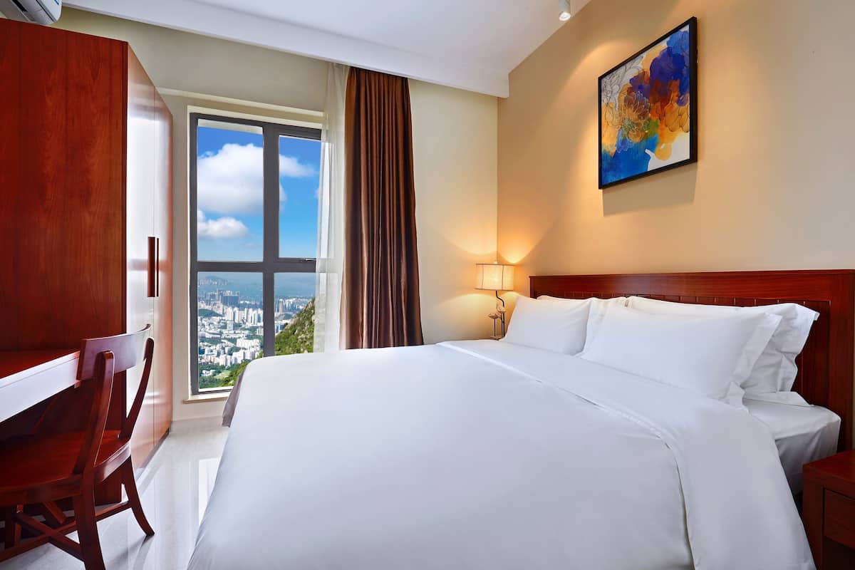 Habitación de hotel con una cama grande, un escritorio y vistas a un paisaje urbano a través de una ventana.