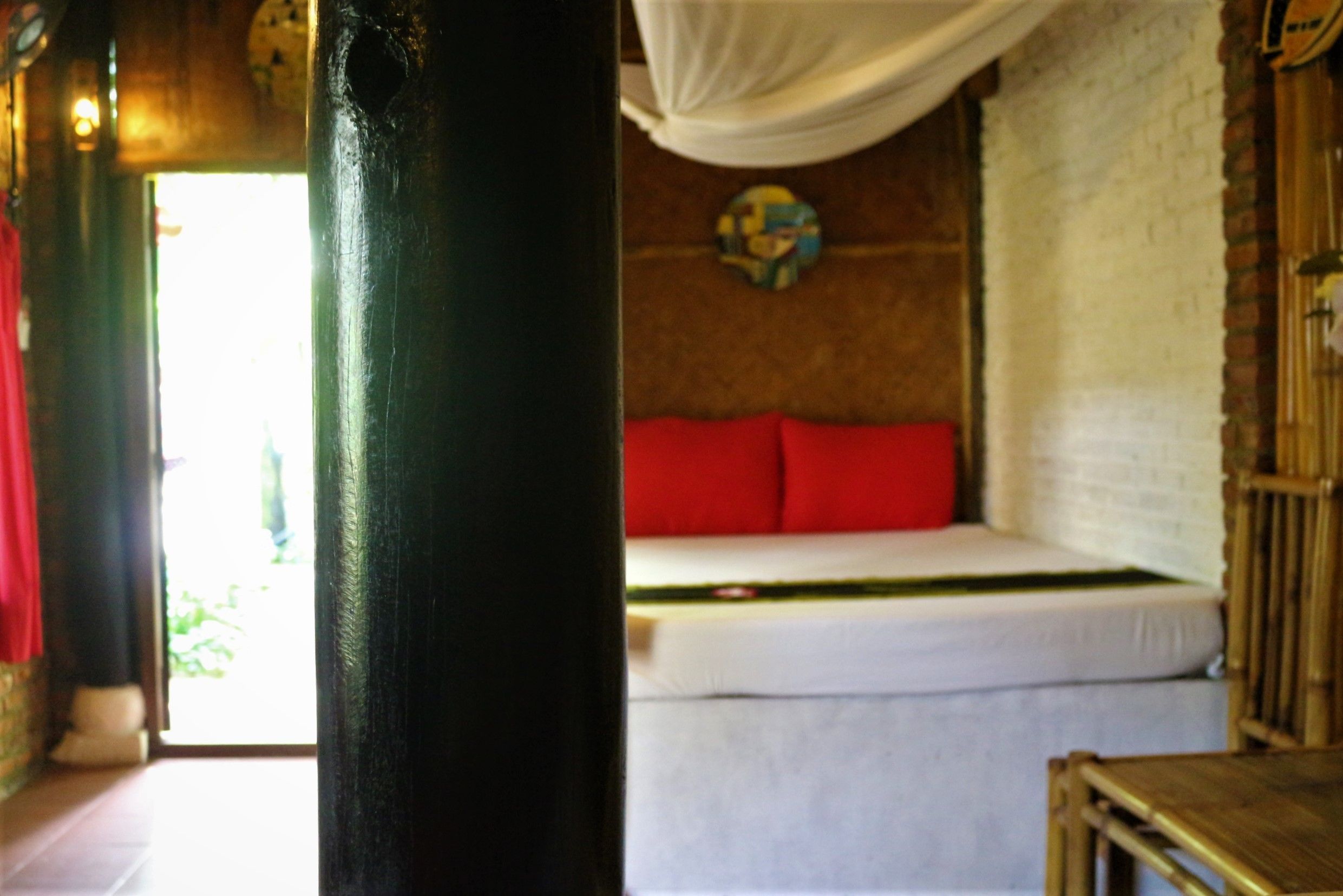 Une pièce avec un lit, un rideau blanc, une chaise en bois et un mur en briques.