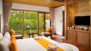 A hotel room with a large bed, a TV, a wooden desk, and a view of lush greenery. - Khmer House Resort (Siem Reap)