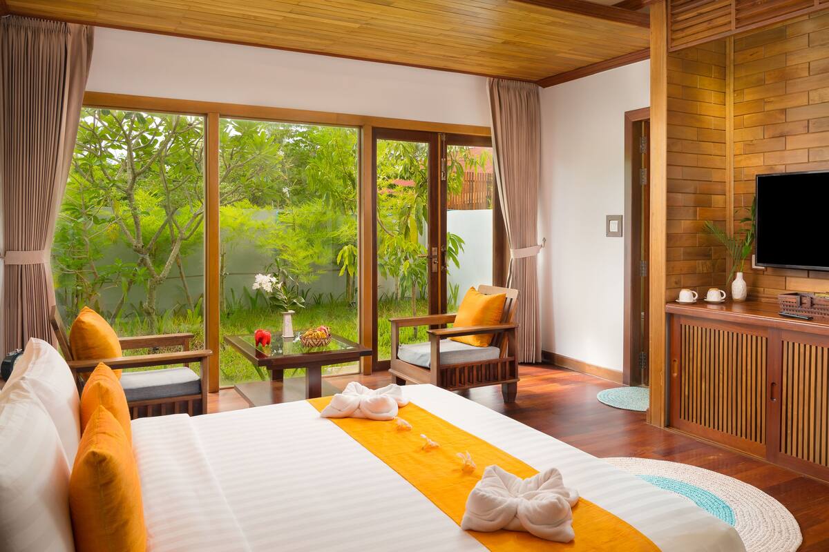 Une chambre d’hôtel avec un grand lit, une télévision, un bureau en bois et une vue sur une végétation luxuriante.