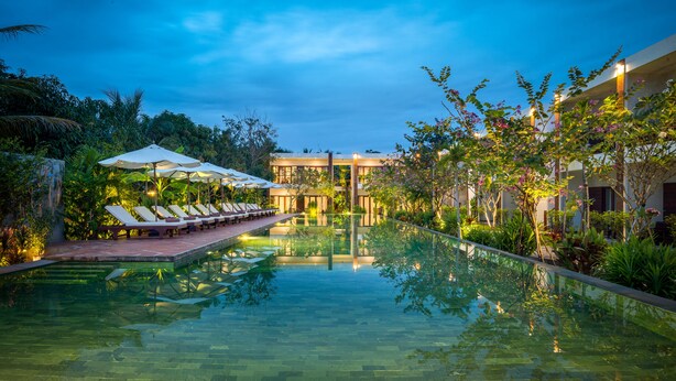 A serene pool area with lounge chairs and umbrellas, surrounded by lush greenery and modern architecture. - Khmer House Resort (Siem Reap)