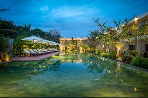 A serene pool area with lounge chairs and umbrellas, surrounded by lush greenery and modern architecture.