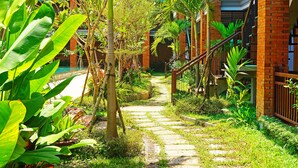 A pathway leading to a building with a brick facade, surrounded by lush greenery and palm trees. - Khmer House Resort (Siem Reap)