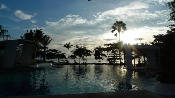 Piscina com palmeiras e vista para o pôr do sol.