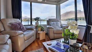 A modern living room with two leather sofas, a coffee table, and a view of a lake and mountains through large windows. - Amazing Queenstown Guesthouse (Queenstown)