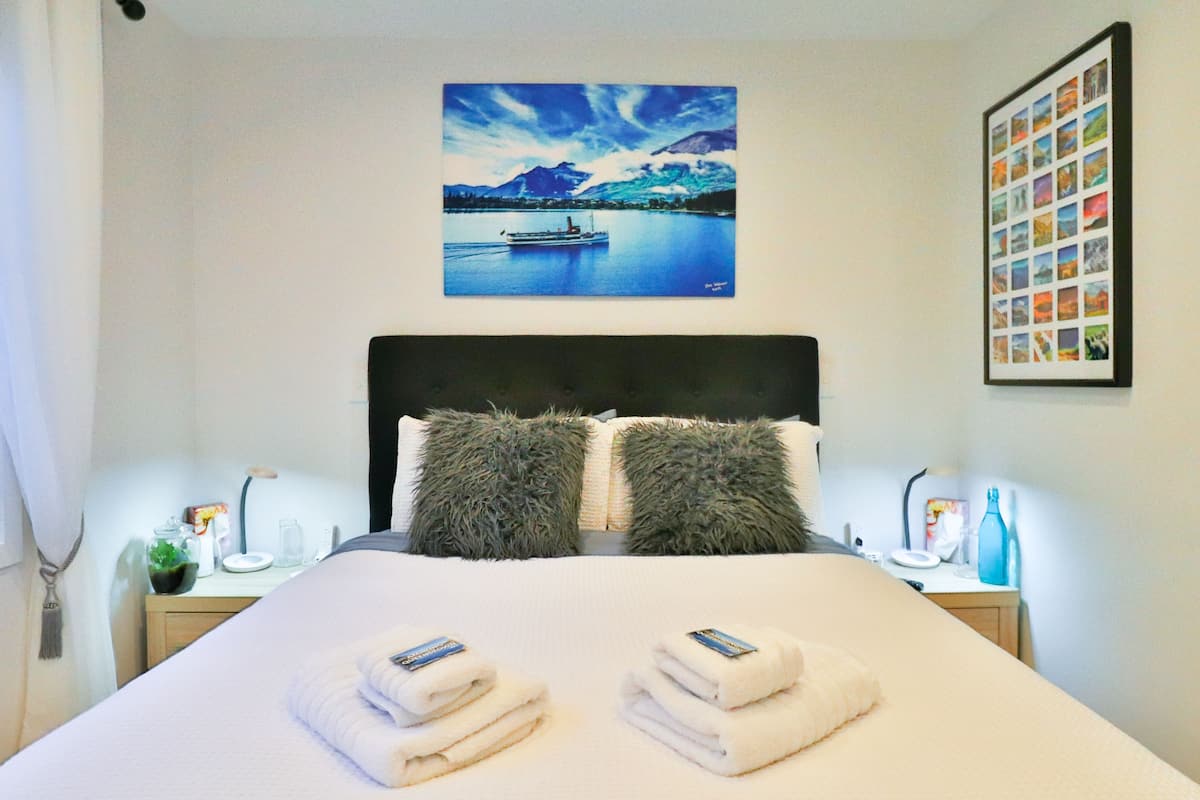 A neatly made bed with two pillows, a framed landscape painting above, and a photo collage on the wall.