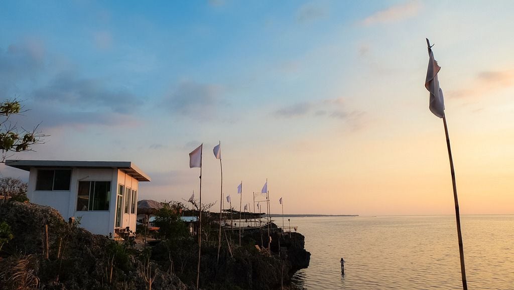 Una propiedad costera con un edificio blanco moderno, banderas y vista al mar.
