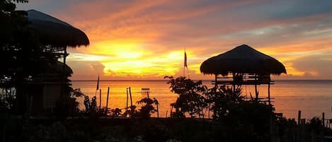 A sunset view with a beach and thatched-roof structures.
