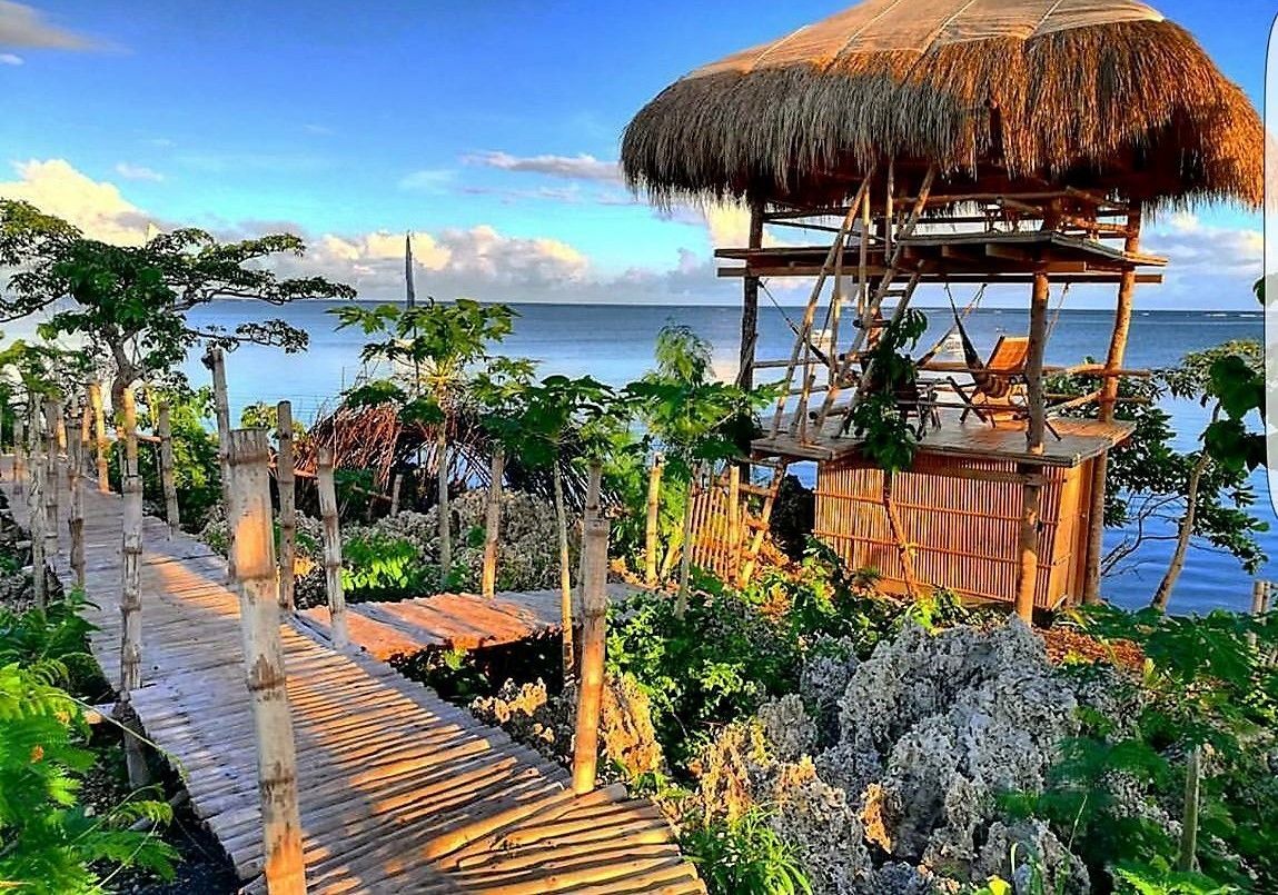 Une terrasse en bois mène à une construction au toit de chaume, d’où l’on peut admirer l’océan.