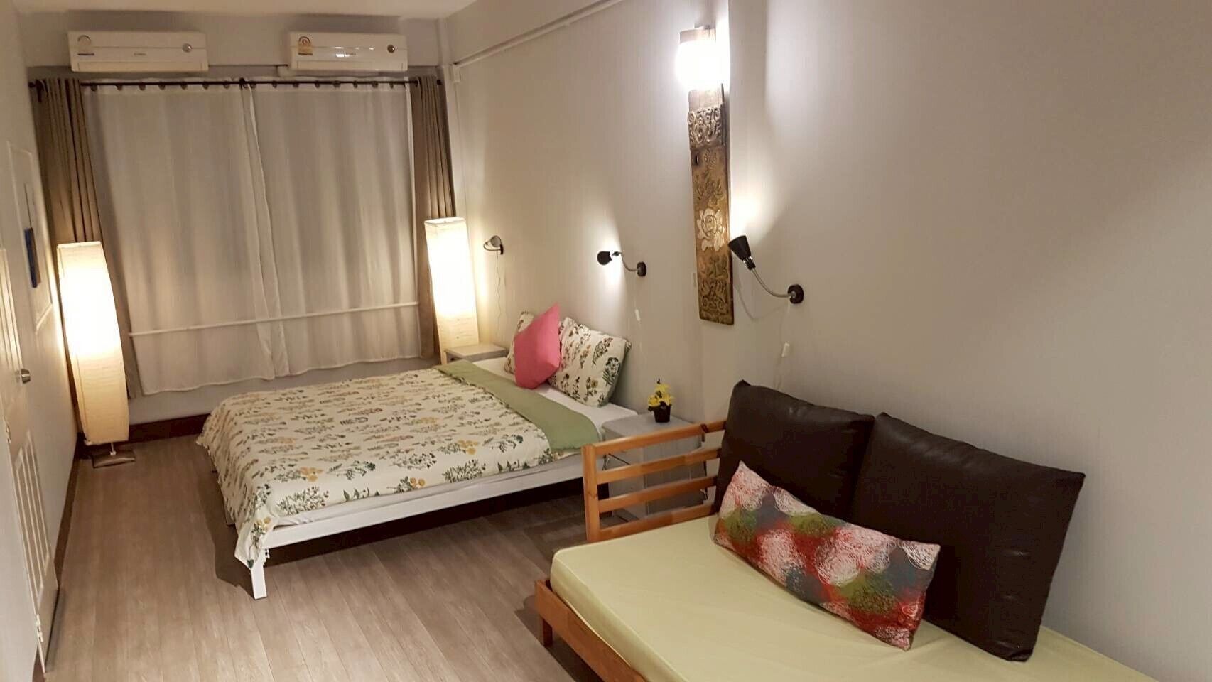 A bedroom with a bed, a sofa, a nightstand, a lamp, and a wall-mounted light fixture.