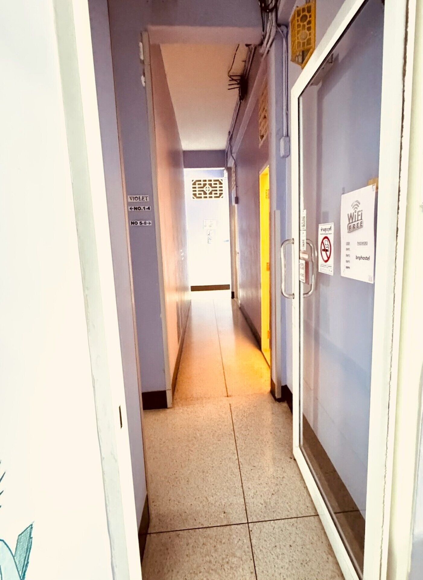 Un pasillo con puertas identificadas con violeta y números del 1 al 4, un cartel de prohibido fumar y un símbolo de WiFi.