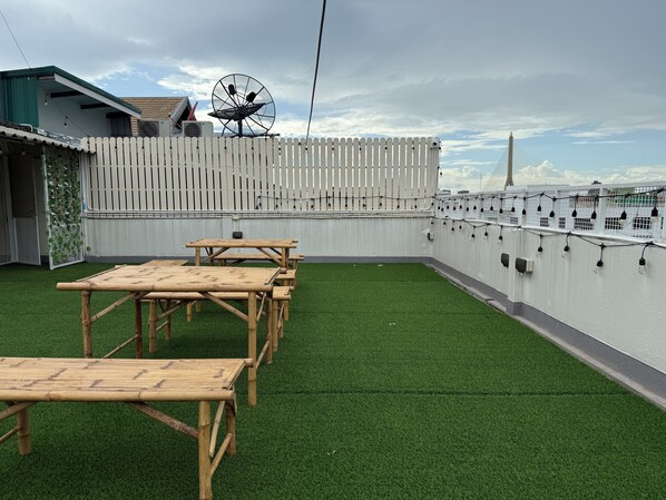 Una terraza en la azotea con césped artificial, mesas de madera, una valla blanca y una antena parabólica.