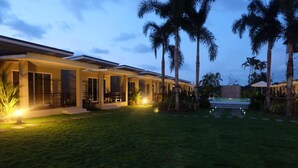 A modern hotel with a covered outdoor area, palm trees, and a well-lit lawn. - The Oasis Khaolak Resort (Takua Pa)