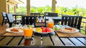 A breakfast table with plates of food, drinks, and condiments on a wooden deck overlooking lush greenery. - The Oasis Khaolak Resort (Takua Pa)