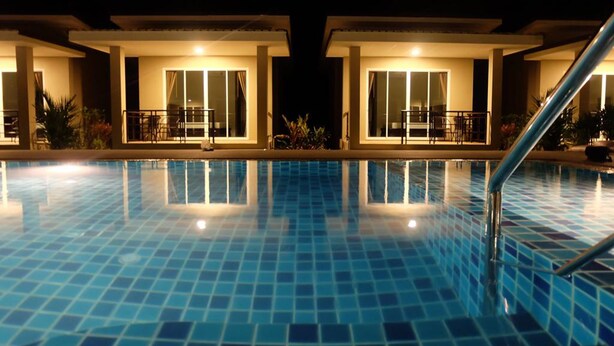 A swimming pool with a tiled floor and a railing, surrounded by two buildings with balconies and large windows. - The Oasis Khaolak Resort (Takua Pa)