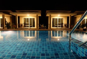 Uma piscina com piso revestido e corrimão, rodeada por dois edifícios com varandas e grandes janelas.