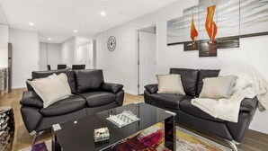 A modern living room with two black leather sofas, a glass coffee table, and a large abstract painting on the wall. - Astra Apartments Newcastle West (Newcastle West)