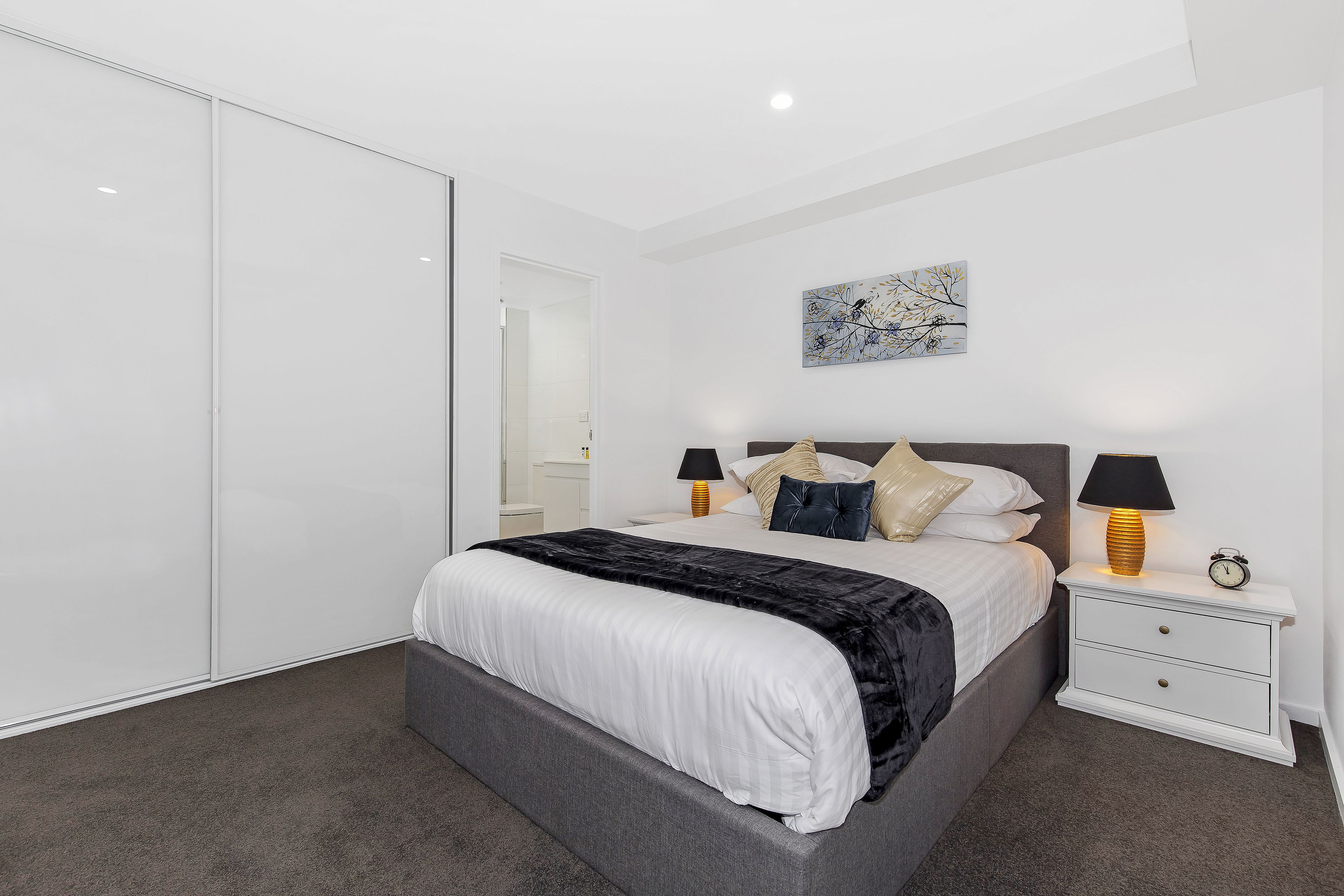 A bedroom with a bed, bedside tables, a wardrobe, and a painting on the wall.