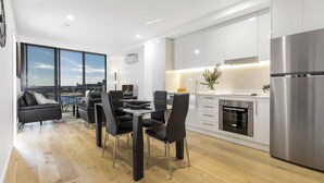 A modern kitchen with stainless steel appliances, a dining area with a glass table, and a view of the city through large windows. - Astra Apartments Newcastle West (Newcastle West)