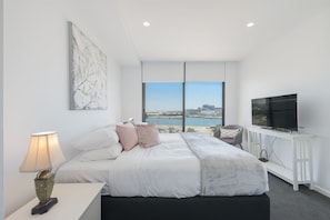 A modern bedroom with a large bed, a TV, and a view of a cityscape through large windows. - Astra Apartments Newcastle West (Newcastle West)