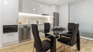 A modern kitchen with white cabinets, stainless steel appliances, and a glass dining table with black chairs. - Astra Apartments Newcastle West (Newcastle West)
