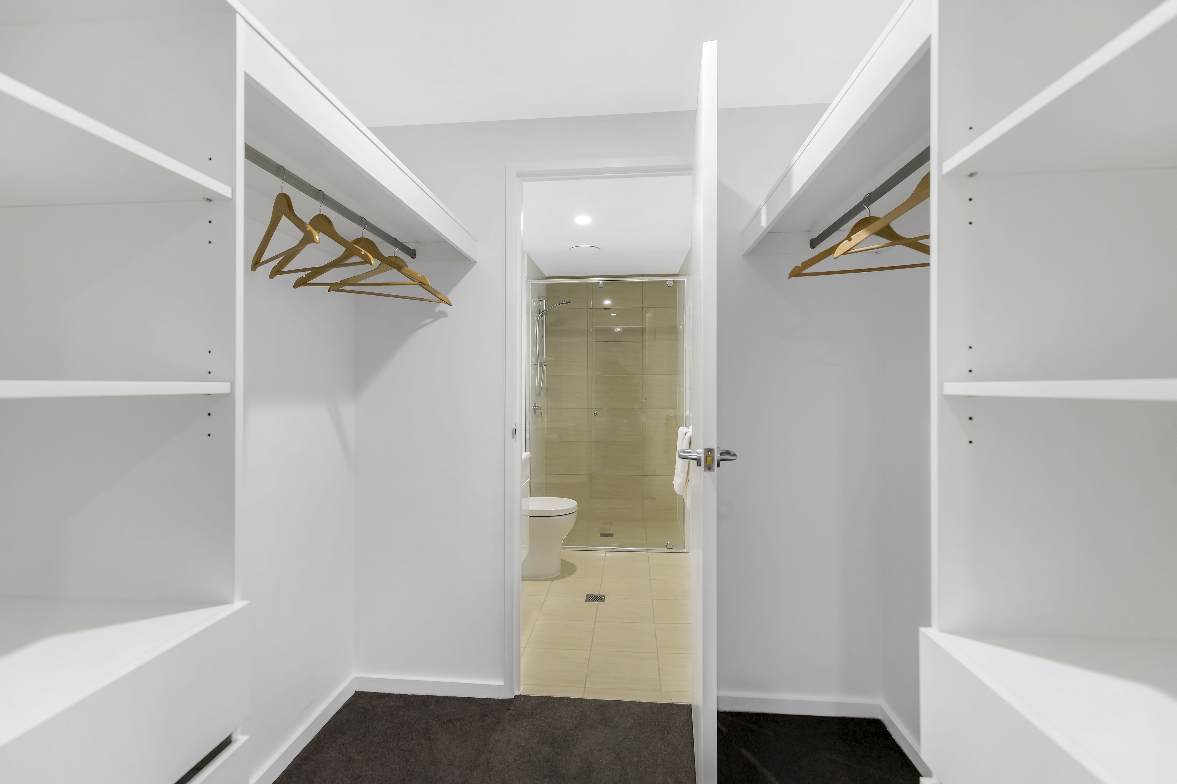 A walk-in closet with open doors, a shower area, and a toilet visible through the glass door.
