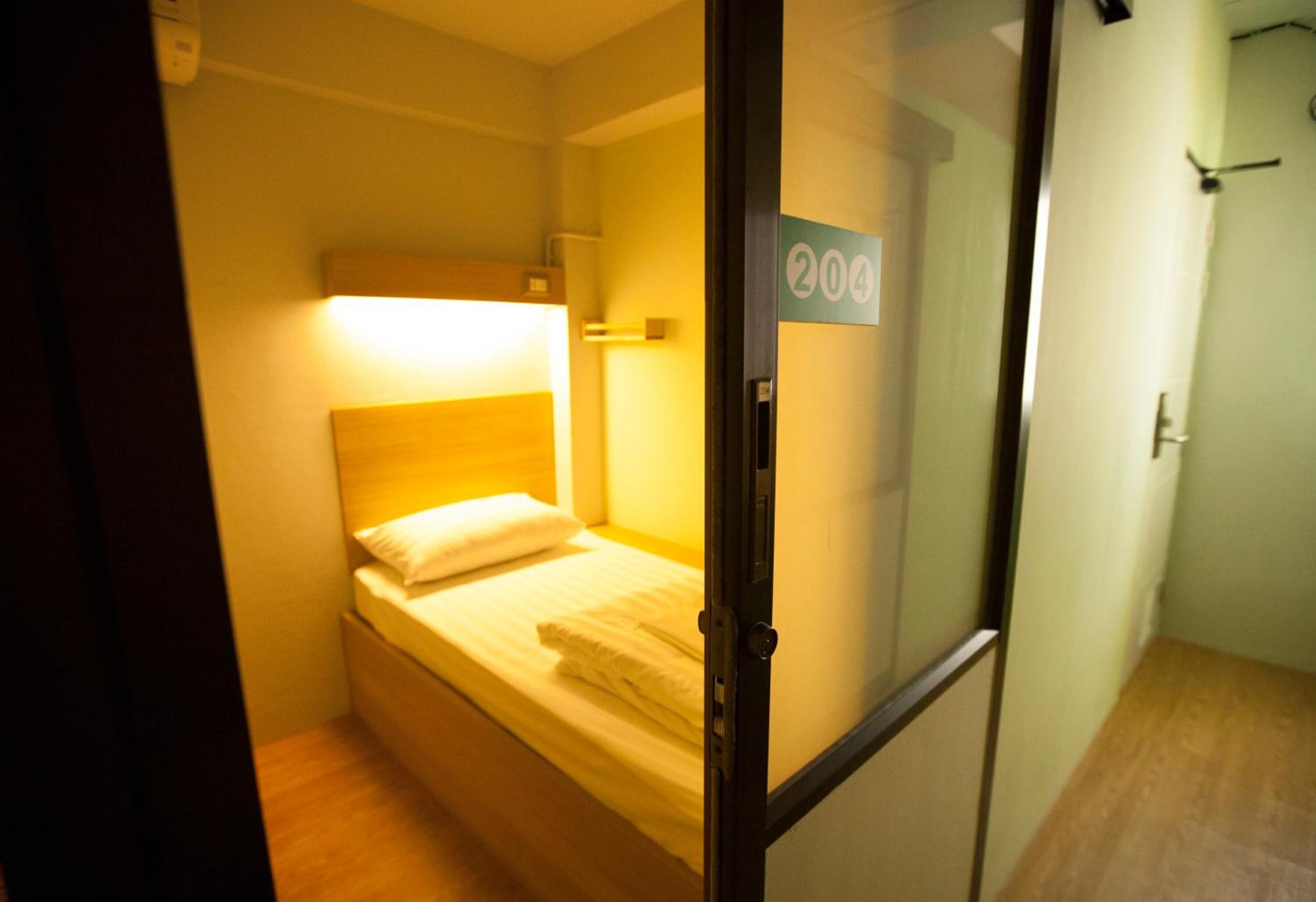 A small, single-bed room with a wooden headboard, a bedside table, and a sign indicating room number 204.