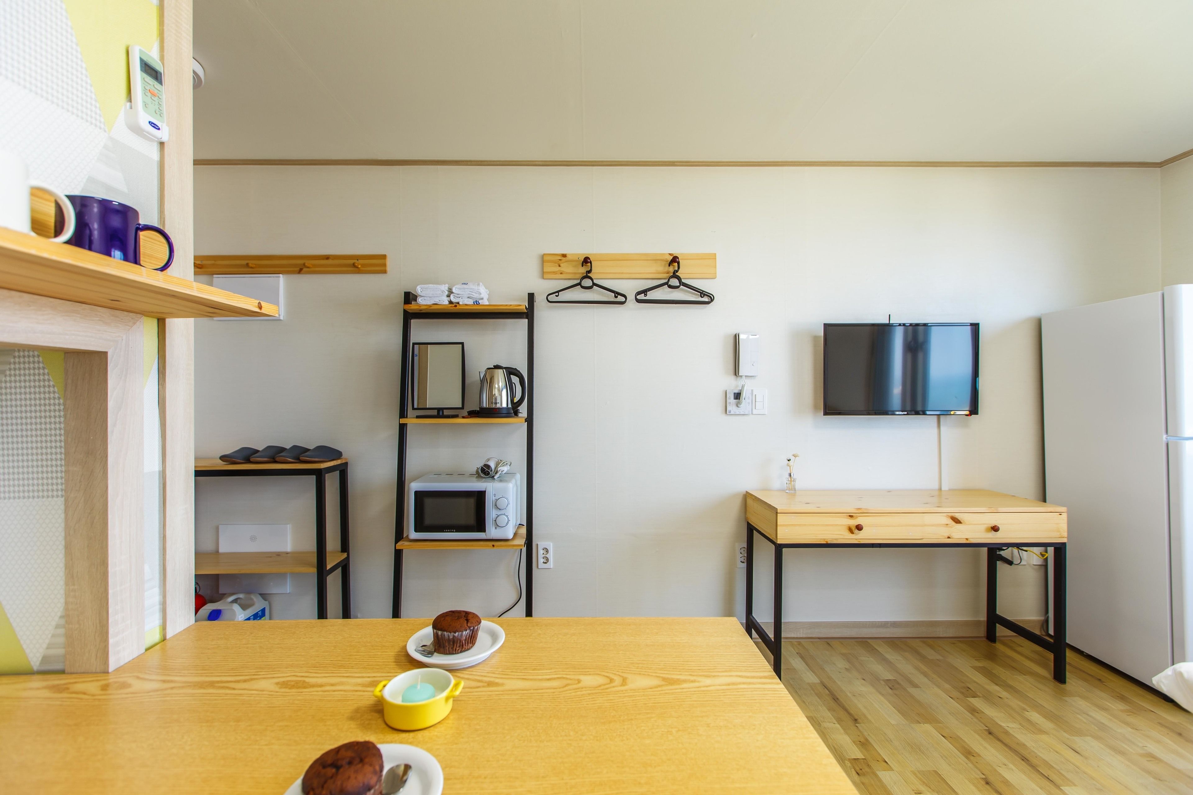 A compact kitchen with a wooden table, microwave, and hanging clothes rack.