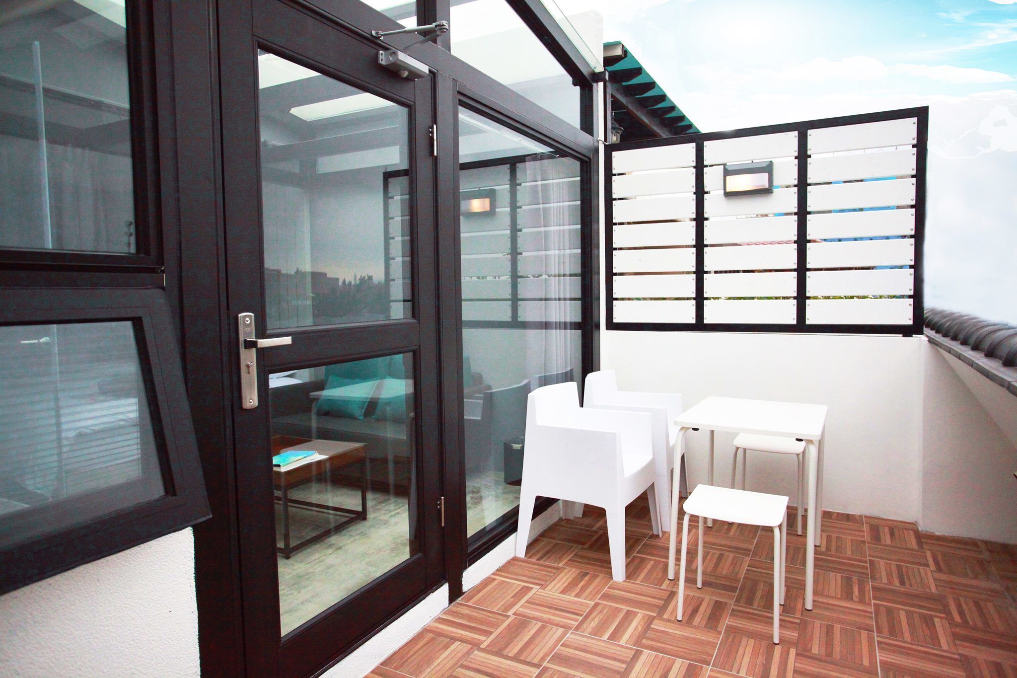 Un balcon avec une porte vitrée, des chaises blanches et une petite table.