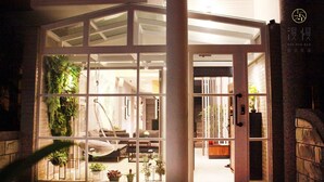 A hotel entrance with a glass door, indoor plants, and a hanging chair. - ManMan (Hualien City)