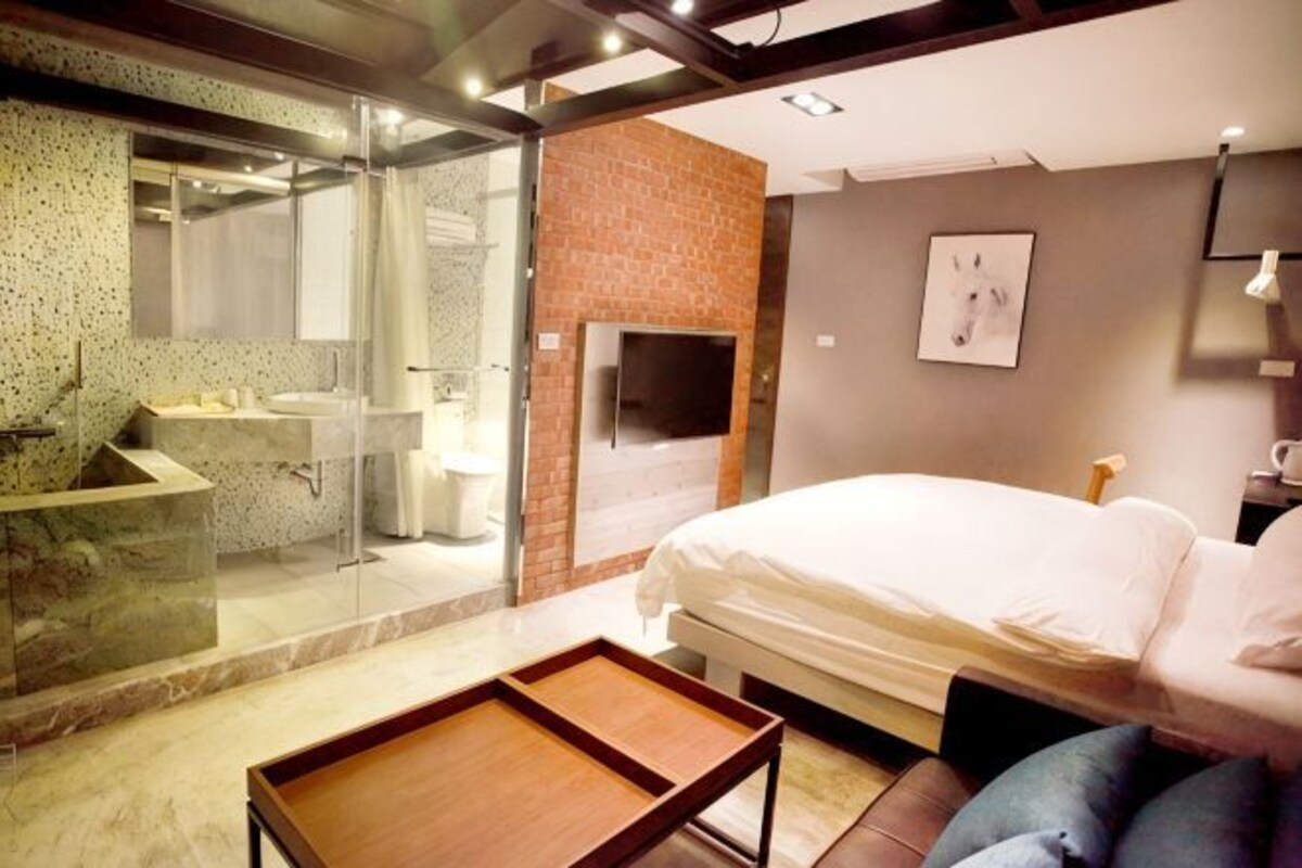 Un dormitorio moderno con cama, un baño con paredes de cristal y una pared de ladrillo decorativa.