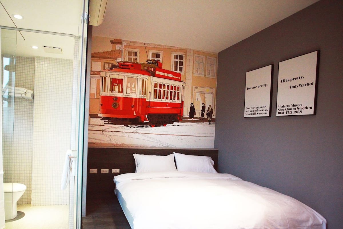 A hotel room with a bed, a glass shower enclosure, and a wall mural of a tram.