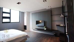 A modern bedroom with a bed, a TV mounted on the wall, a window, and a shelf with items. - ManMan (Hualien City)