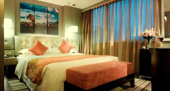 Une chambre d’hôtel avec un grand lit, une table de chevet, une commode, une lampe, une fenêtre avec des rideaux et un tableau au mur.