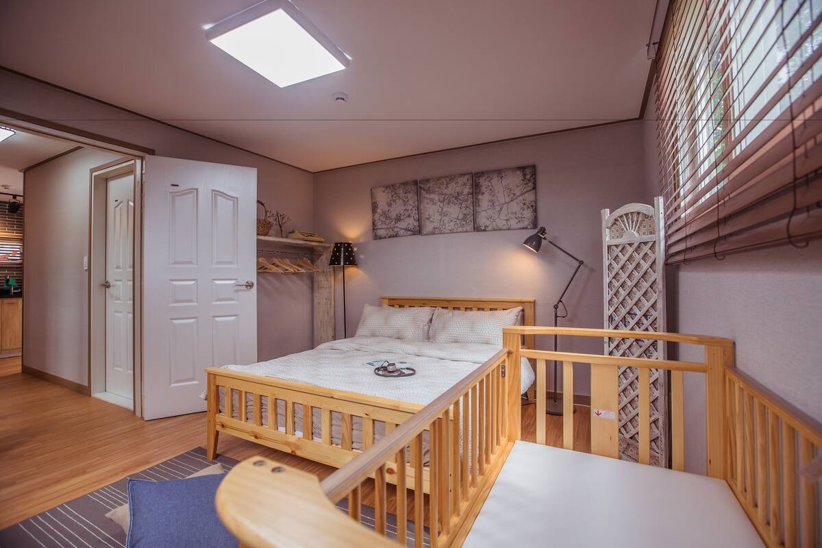 Un dormitorio con cama de madera, escritorio, silla, armario y ventana con persianas.