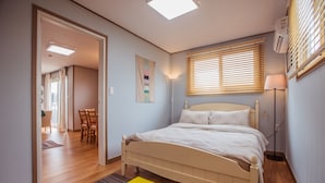 Une chambre à coucher avec un lit, une lampe de chevet, une fenêtre avec des stores et une porte donnant sur une autre pièce.