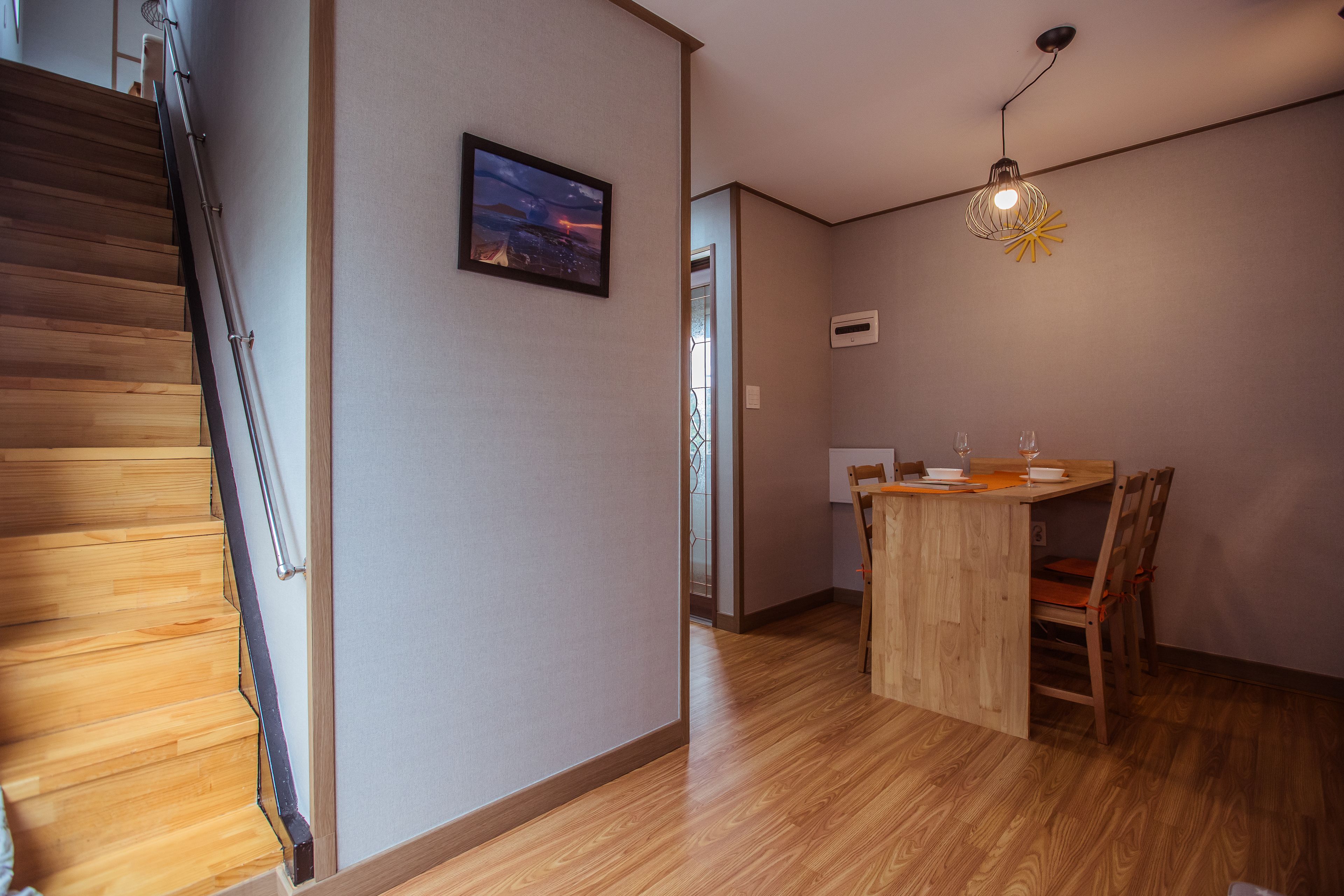 A wooden staircase, a dining area with a wooden table and chairs, and a hanging light fixture.