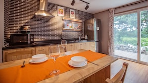 Une cuisine moderne avec un mur recouvert de briques, des appareils en acier inoxydable et un coin repas comprenant une table et des chaises en bois.