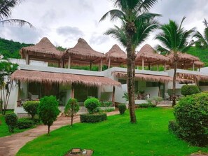 Un resort con varias construcciones de techo de paja, abundante vegetación y un jardín cuidado.