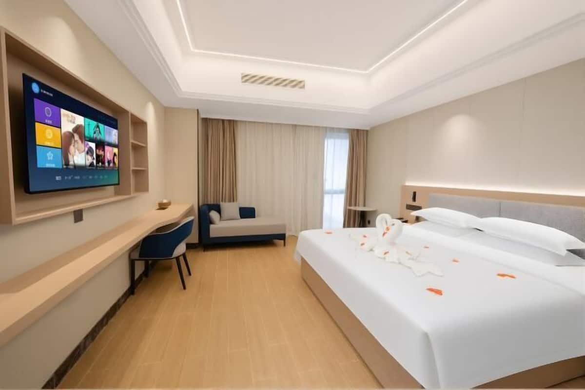 Une chambre d’hôtel avec un lit, un bureau, une chaise, une télévision et une fenêtre avec des rideaux.