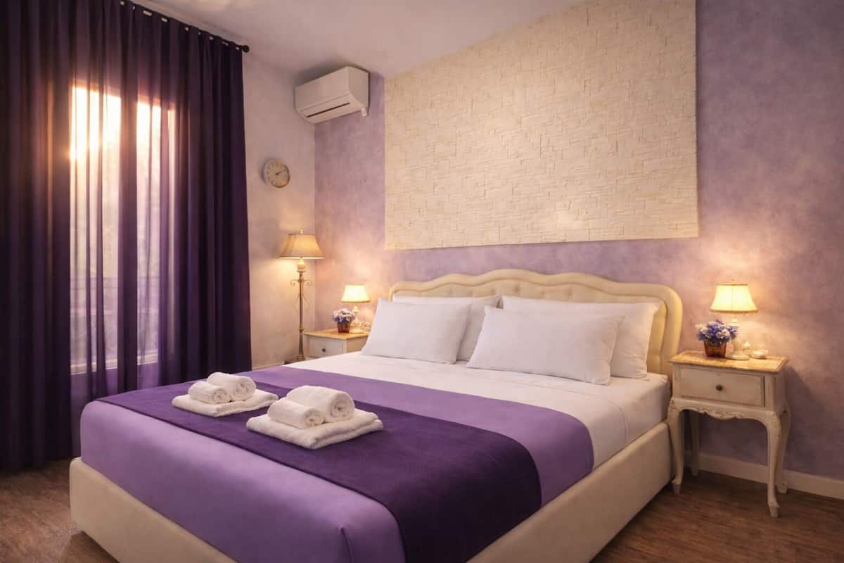 Una habitación de hotel con una cama, dos mesitas de noche, un reloj de pared y un equipo de aire acondicionado.