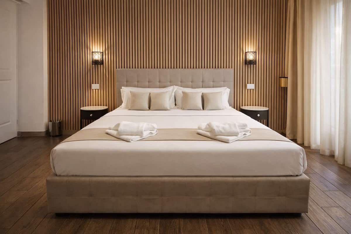 Una cama grande con cabecera capitonada, dos mesitas de noche y un muro de listones de madera.