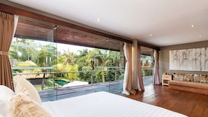 Een moderne slaapkamer met een groot bed, een glazen wand en uitzicht op een zwembad en tropische tuin.