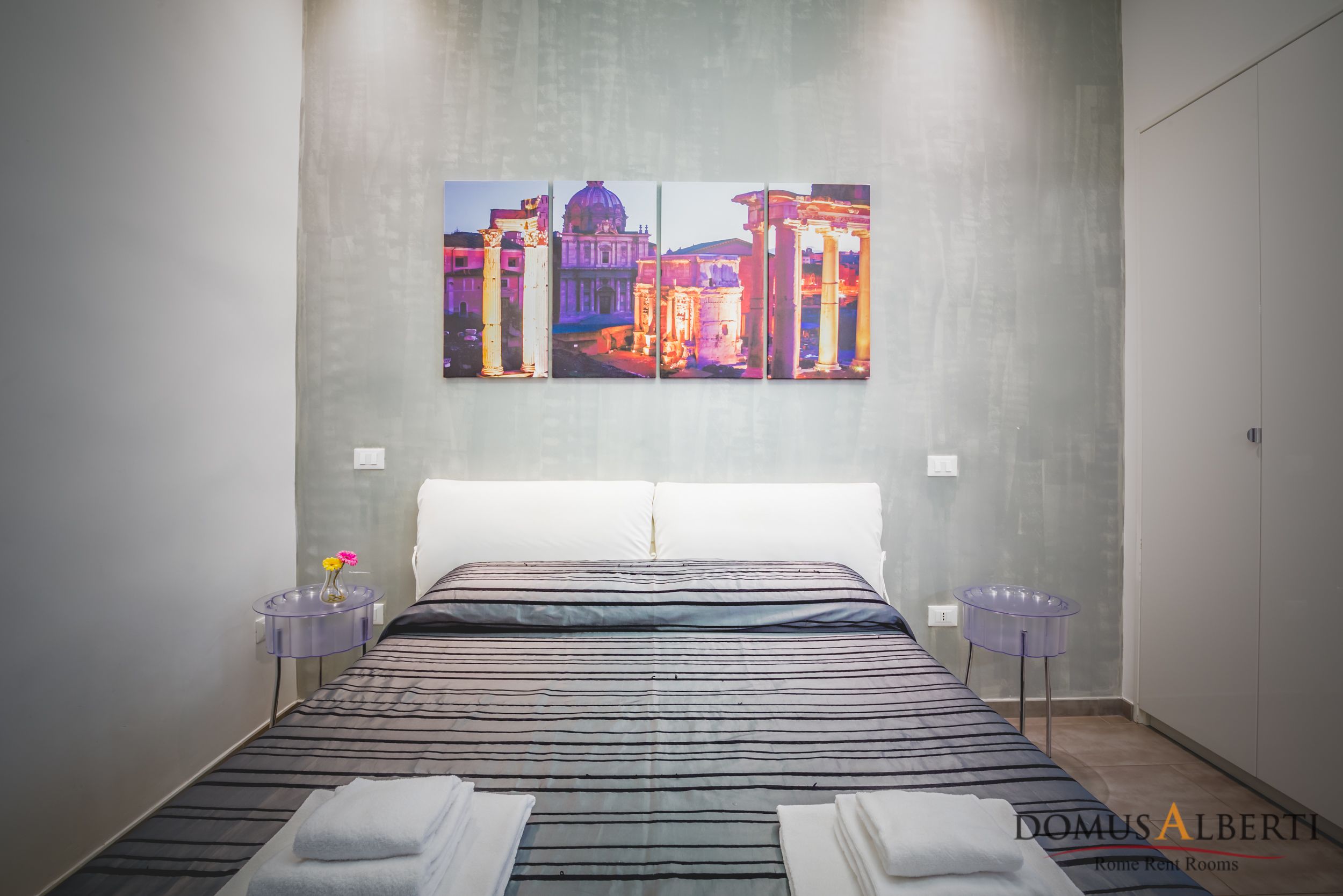 Ein Hotelzimmer mit einem großen Bett, einem an der Wand befestigten Kunstwerk, zwei Nachttischen mit Lampen und einem Kleiderschrank.