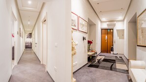 A hotel hallway with a carpeted floor, framed pictures on the walls, and a wooden door at the end. - Domus Alberti (Rome)