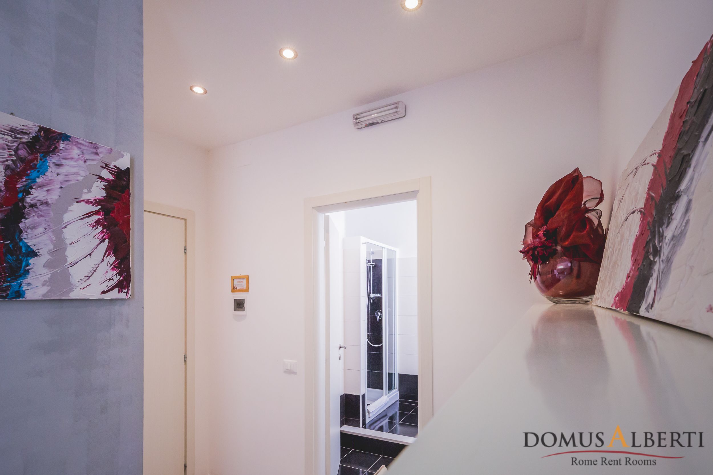 Een moderne hotelhal met een glazen douchedeur, abstracte kunst aan de muren, en een logo voor DOMUS ALBERTI Rome Rent Rooms.