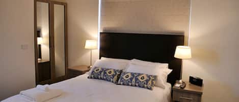 A hotel room with a large bed, two bedside lamps, a nightstand, and a mirror.