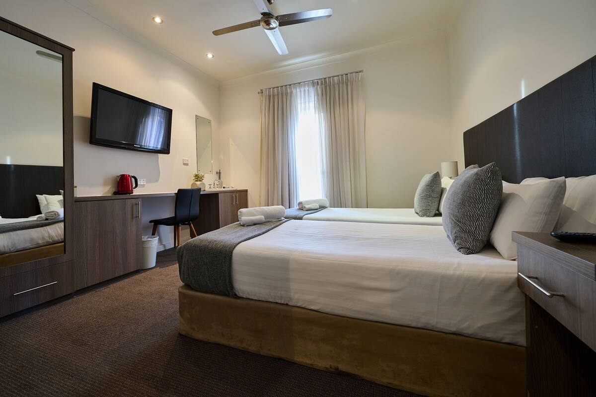 Ett hotellrum med en säng, ett skrivbord, en stol, en tv och en takfläkt.